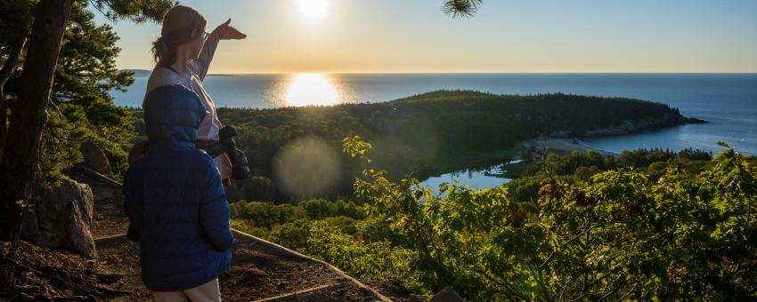 A family hiking with a view of the Atlantic and a rising sun from The Beehive Trail in Acadia National Park.